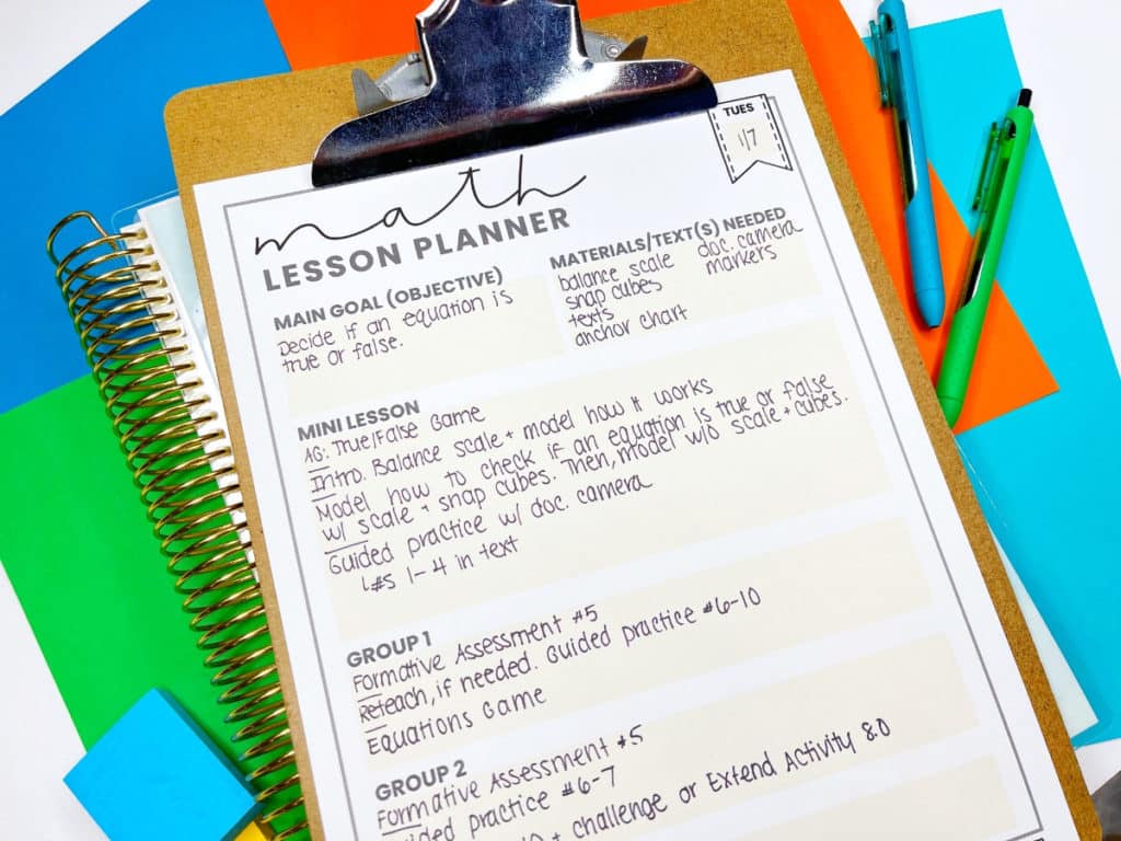 Lesson planner for planning a math lesson on a clipboard, with a notebook and pens.