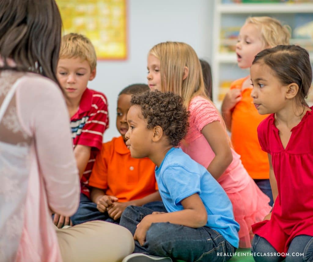 a teacher sharing a book with a group of students on the rug