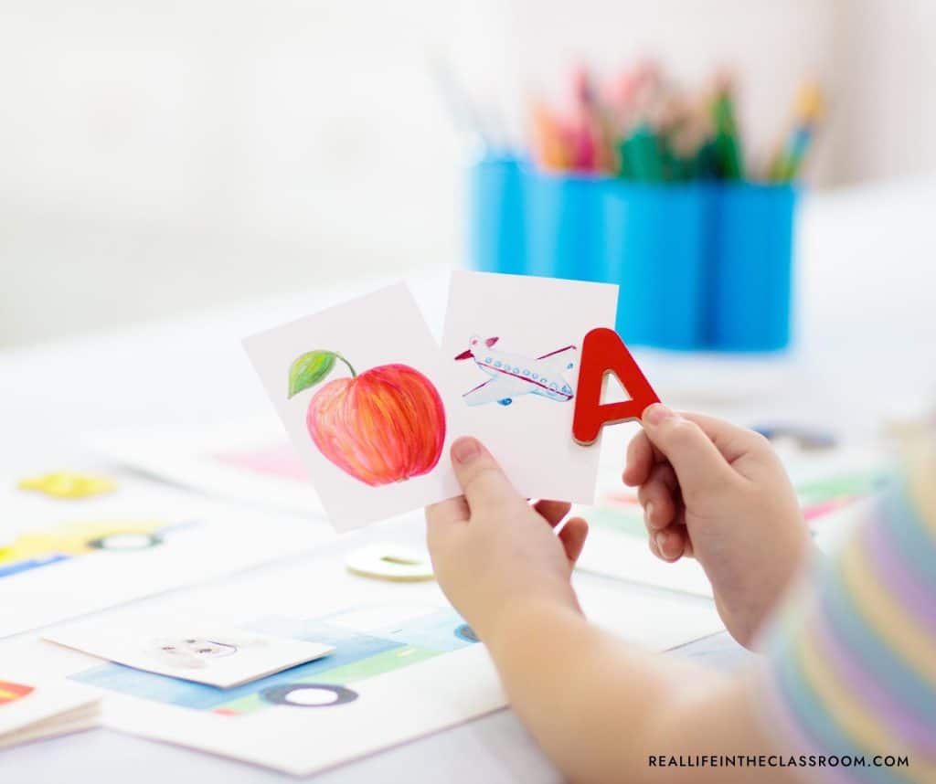 A child's hands holding a letter A magnet and two flash cards with an apple and an airplane
