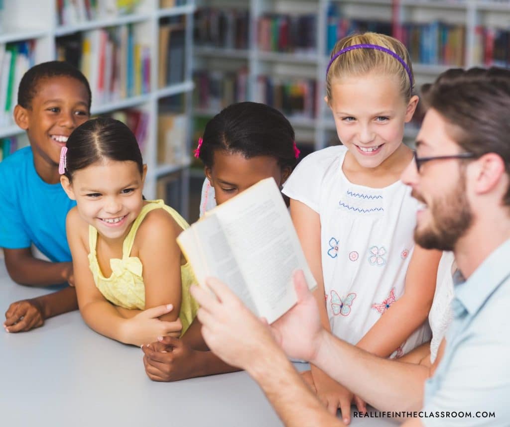 a male teacher reading a book to a group of students
